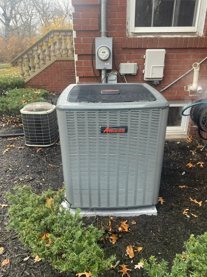 A new Amana condenser beside a brick house, with the old unit next to it